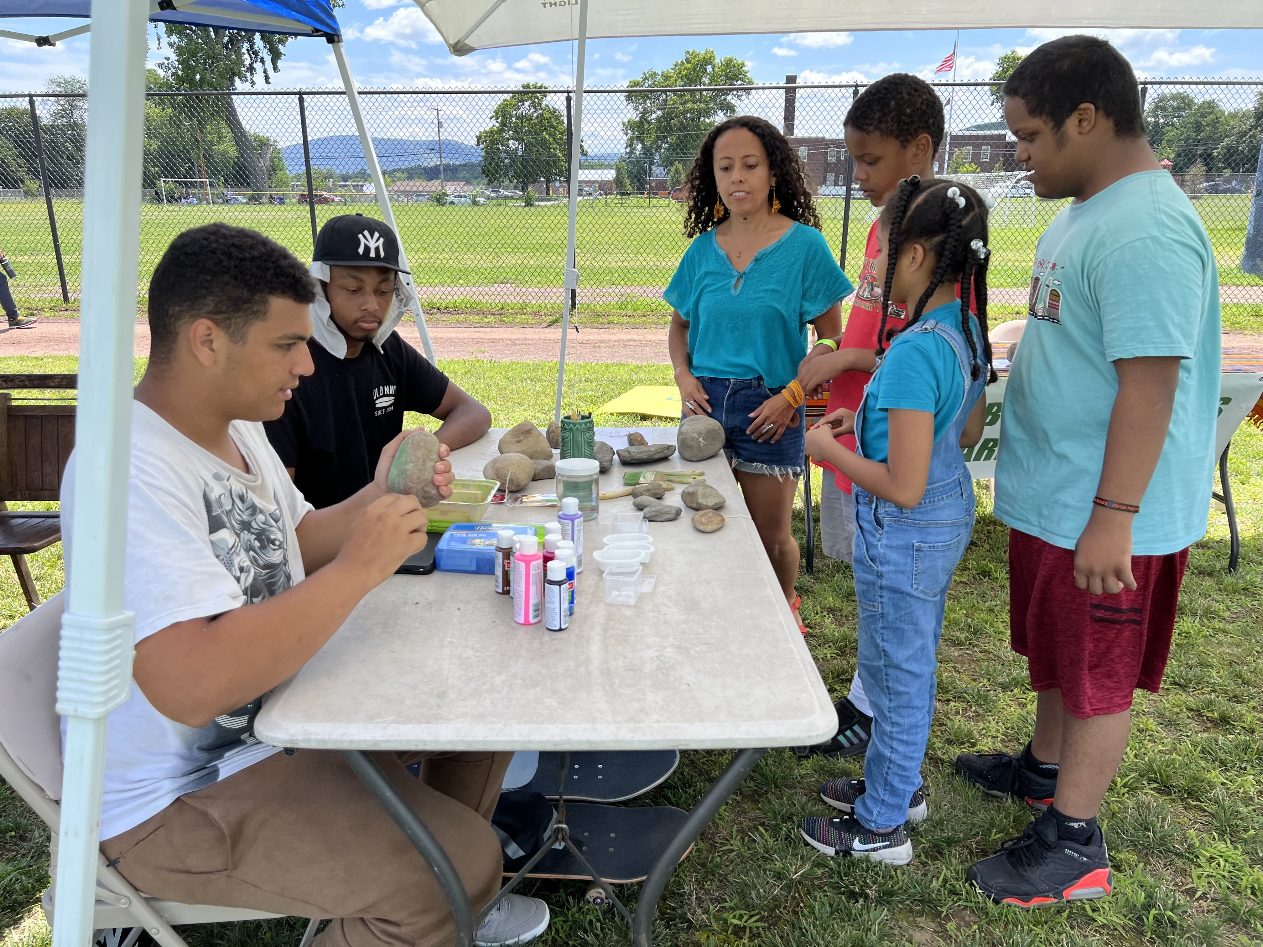 Betty Bastidas y sus jóvenes aprendices pintan con miembros de la comunidad en mesas.  