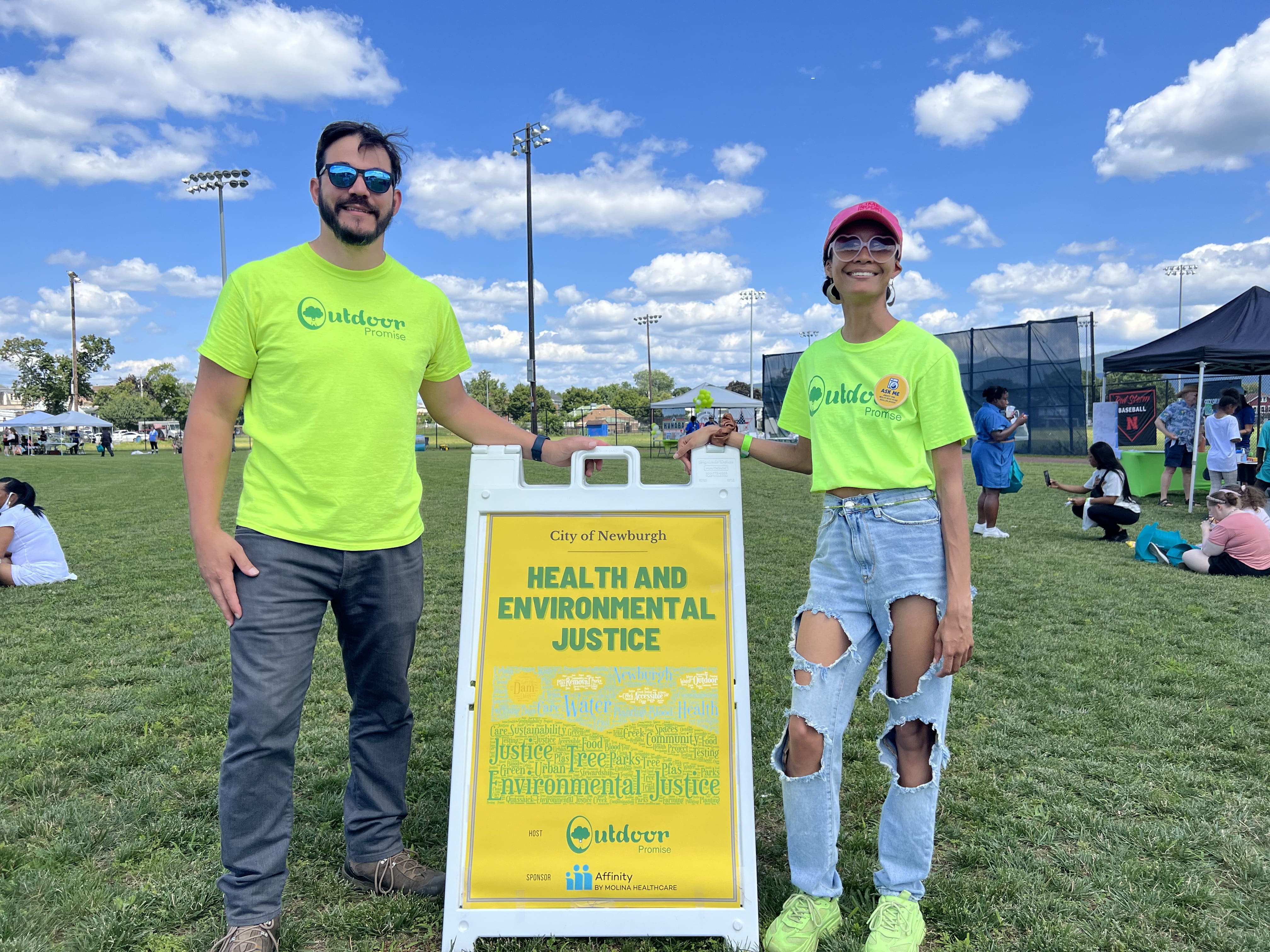 Ronald Zorrilla y Kathryn McKenzie de pie junto al cartel de Salud y Justicia Ambiental en el evento Love Our City de la ciudad de Newburgh